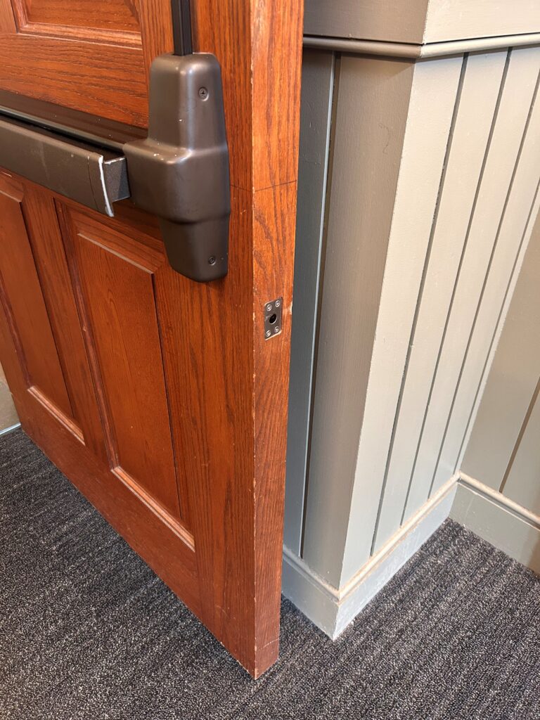 Ryan Krakowsky sent me today's Fixed-it Friday photos of an improper installation of an auxiliary fire pin for less-bottom-rod fire exit hardware.  Do you know the correct mounting location?